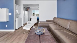 Un salon moderne avec un canapé beige, un fauteuil blanc, une table basse en bois et un téléviseur fixé au mur.