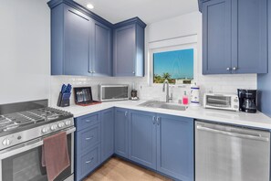 Une cuisine moderne avec des meubles bleus, des appareils en acier inoxydable et une fenêtre donnant sur des palmiers.