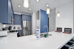 Une cuisine moderne dotée d’appareils électroménagers en acier inoxydable, d’un plan de travail blanc et de meubles de couleur bleue.