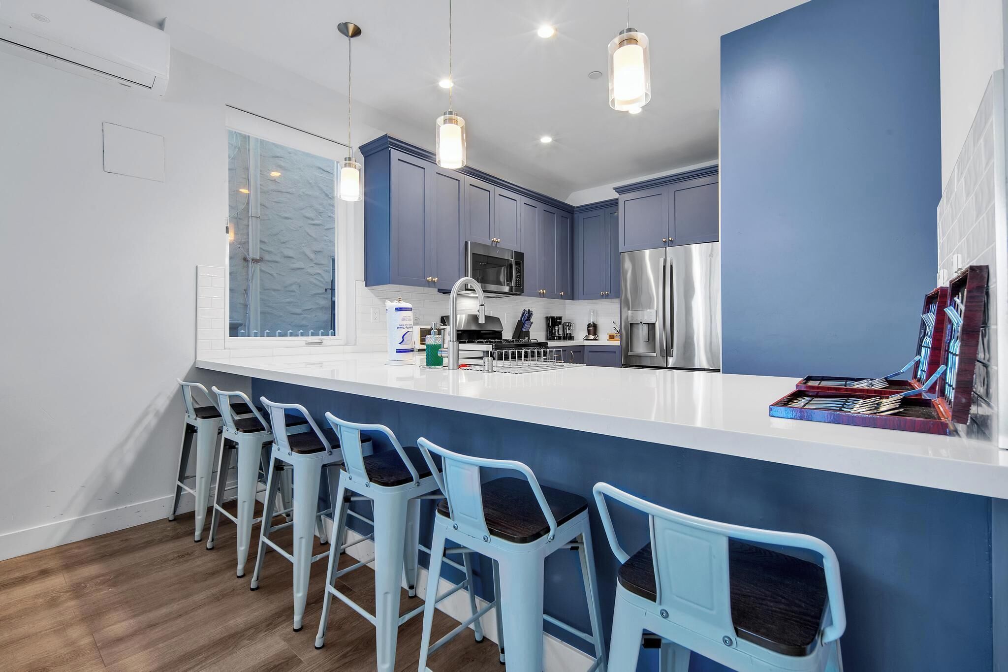 A modern kitchen with blue cabinets, a white countertop, and a bar area with light blue bar stools.