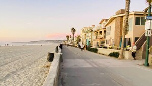 Uma estrada costeira com uma praia arenosa de um lado e uma fileira de edifícios altos com varandas e áreas de estar ao ar livre.