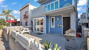 A two-story house with a patio, a barbecue grill, and a white fence.