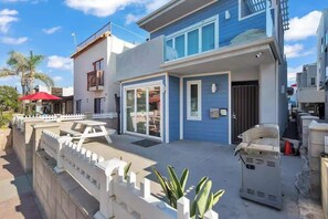 A two-story house with a patio, a barbecue grill, and a white fence.