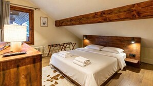 Un dormitorio con cabecera de madera, cama con sábanas blancas, un escritorio de madera con lámpara y una alfombra de cuero de vaca.