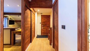 Un pasillo con suelo de madera y puertas, que conduce a una habitación con un escritorio y una computadora.
