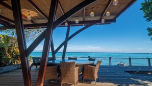 Uma área de estar coberta ao ar livre, com móveis de vime e vista para o mar.