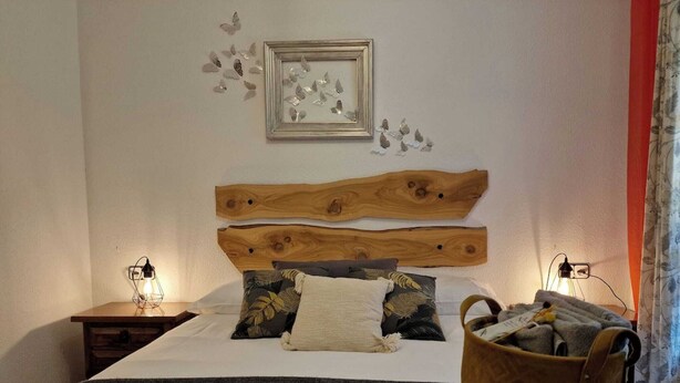 Quarto com cabeceira de madeira, cama com roupa de cama estampada, duas luminárias de cabeceira e mesa de cabeceira com abajur.