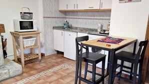 Uma cozinha compacta com armários brancos, micro-ondas, pia e uma pequena mesa com cadeiras.