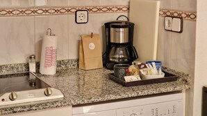 Uma bancada de cozinha com uma cafeteira, um porta-papel toalha, um pacote de café e uma bandeja com diversos objetos.
