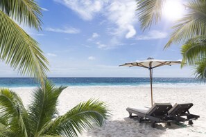 A beach with white sand, a clear blue sky, and a calm sea. There are two lounge chairs and a beach umbrella. - Beautifully renovated Longboat Key Villa brief walk to a private beach (Longboat Key)