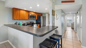 A kitchen with wooden cabinets, a microwave, a refrigerator, and a sign that reads 'Beach Hair Don't Care'. - Walk to Beach, Dining & Shops- Community Pool (Holmes Beach)