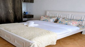 Ein ordentlich bezogenes Bett mit weißem Kopfteil, ein Holzschrank und ein kleiner Nachttisch mit Lampe.