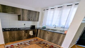 Eine Küche mit dunklen Holzschränken, einem Gasherd, einer Spüle und einem Fenster mit Vorhängen.