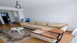 Ein Wohnzimmer mit einem beigen Sofa, einem kleinen weißen Tisch, einem gemusterten Teppich und einem Holztisch.