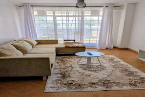 Een woonkamer met een beige bank, een ronde salontafel en een kamerkleed met patroon.