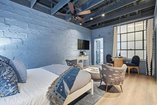 Une chambre avec un mur en briques, un lit recouvert d’une couverture à motifs bleus et blancs, un bureau avec un ordinateur et une chaise.