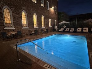 Une piscine avec un bâtiment en briques en arrière-plan, des chaises longues et des tables.
