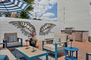 Une terrasse extérieure avec deux chaises, une table, un parasol à rayures et un barbecue.