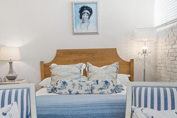 Une chambre à coucher avec une tête de lit en bois, un lit avec une literie bleue et des oreillers à motifs, une table de chevet avec une lampe et un tableau encadré au mur.