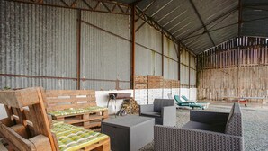 Un espace extérieur aménagé, abrité et doté de mobilier en bois et en osier, d’un foyer et d’une vue sur le paysage environnant.