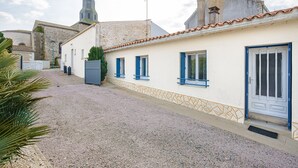 Une rue pavée menant à un bâtiment à la façade blanche et aux volets bleus.