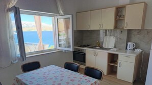 A small kitchen with a table and chairs, a window with a view, and a sink. - Seafront Apartment Valla 5 (Novalja)