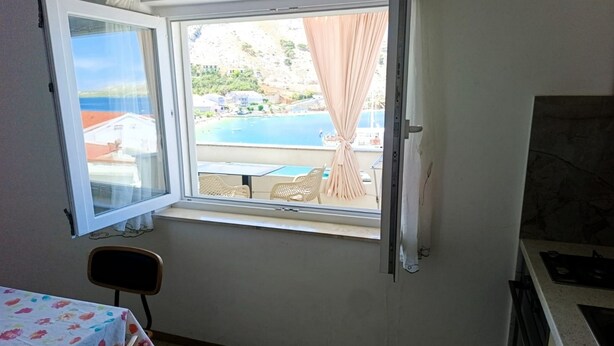 A room with a window overlooking a pool and a view of buildings. There is a table with a floral tablecloth and a chair. - Seafront Apartment Valla 5 (Novalja)