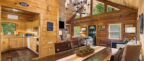 A wooden cabin interior with a kitchen, dining area, and a living room.