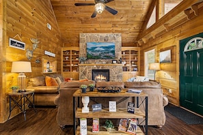 Ein gemütliches Blockhaus-Interieur mit Kamin, Holzwänden, einem darüber montierten Fernseher und einer grünen Tür.
