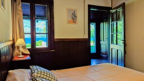 Une chambre à coucher avec un lit, une table de chevet avec une lampe, une fenêtre avec des rideaux et une porte donnant sur l’extérieur.