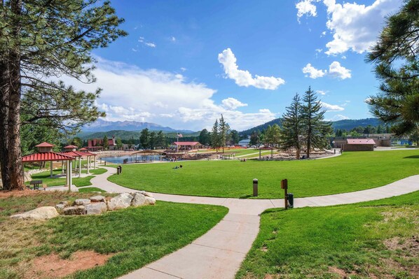 A park with a paved walkway, picnic areas, and a view of mountains in the distance.