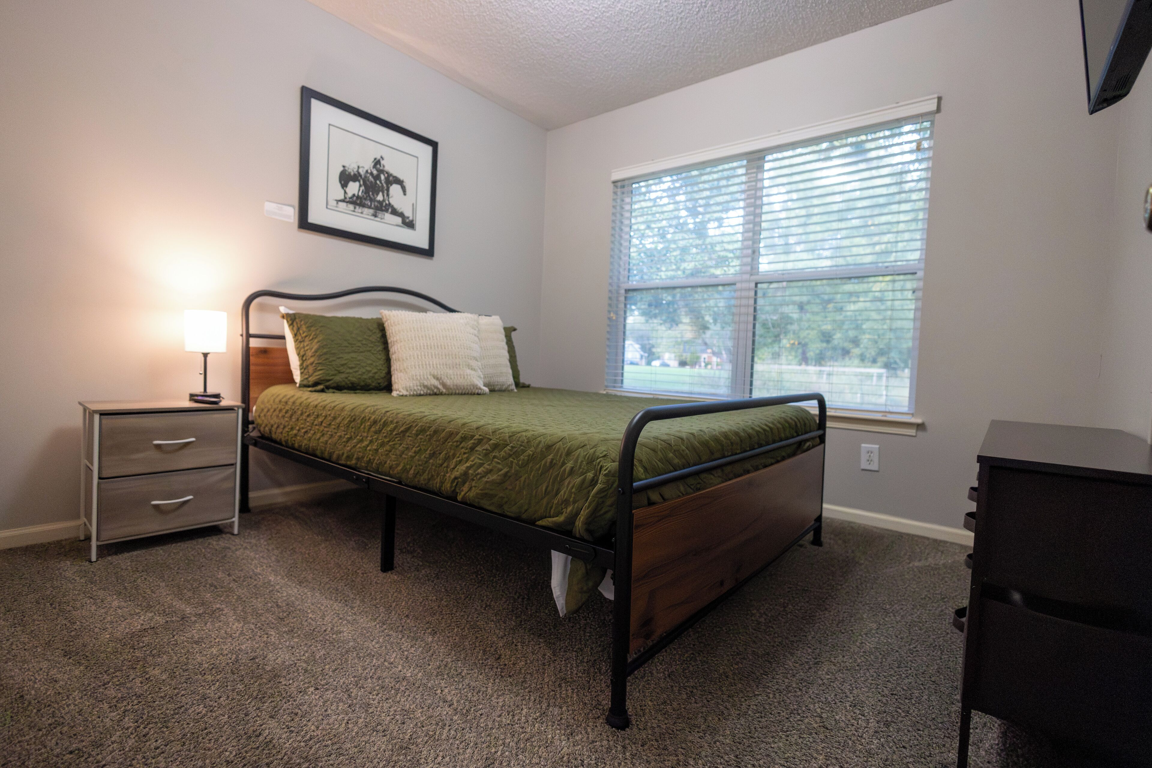 A bedroom with a single bed, a nightstand, a dresser, and a window with blinds.