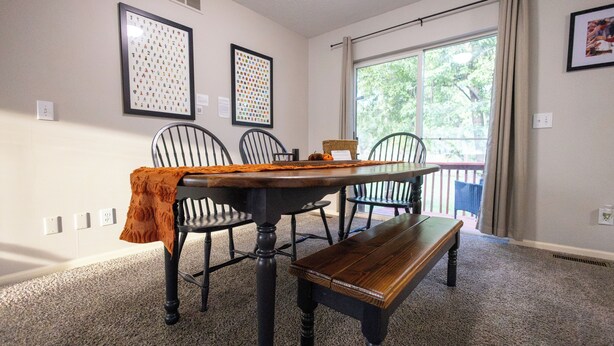 A dining area with a wooden table, four chairs, and a bench. There are two framed pictures on the wall, a window with curtains, and a view of greenery outside. - Full clean 3-bedroom house close to stadiums and pet friendly! (Grandview)