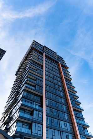 Un edificio moderno e slanciato, con una sporgenza verticale caratteristica, numerosi balconi e un cielo sereno.