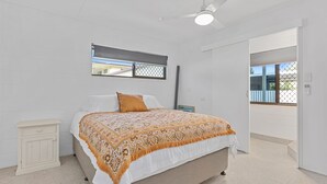 Un dormitorio con cama, mesita de noche, ventana y puerta que da a otra habitación.