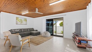 Una sala de estar moderna con un sofá modular gris, techo de madera, pared blanca con un cuadro enmarcado, puerta corrediza de vidrio hacia un balcón y un mueble de televisión de madera con televisor de pantalla plana.