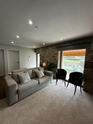 Una sala de estar con un sofá color beige, una silla negra y una pared de piedra.