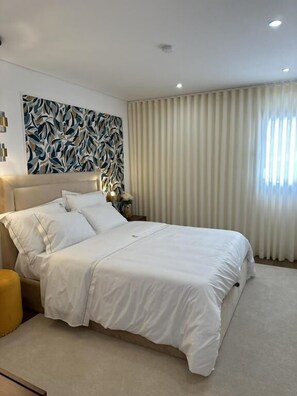 Un dormitorio moderno con una cama grande, cabecera, mesita de noche y una pared con diseño de hojas.