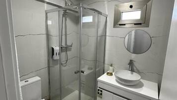 A modern bathroom with a glass-enclosed shower, a toilet, a sink with a mirror, and a white rug on the floor.