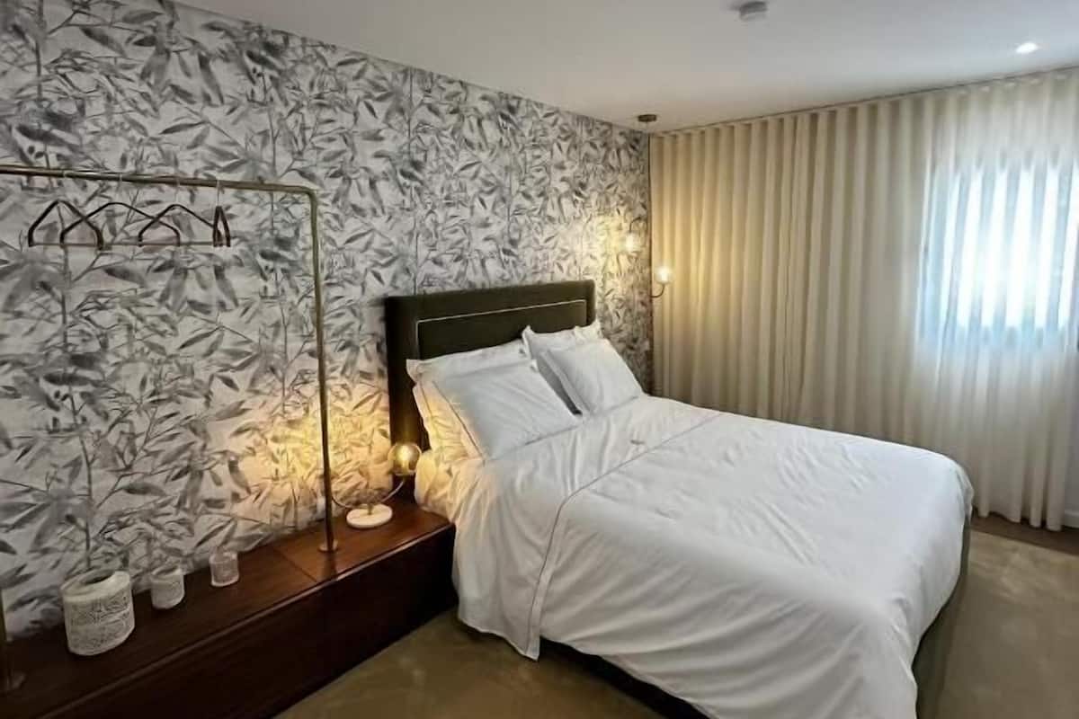 Une chambre à coucher moderne comprenant un lit, une table de chevet, une lampe fixée au mur et un panneau décoratif mural.