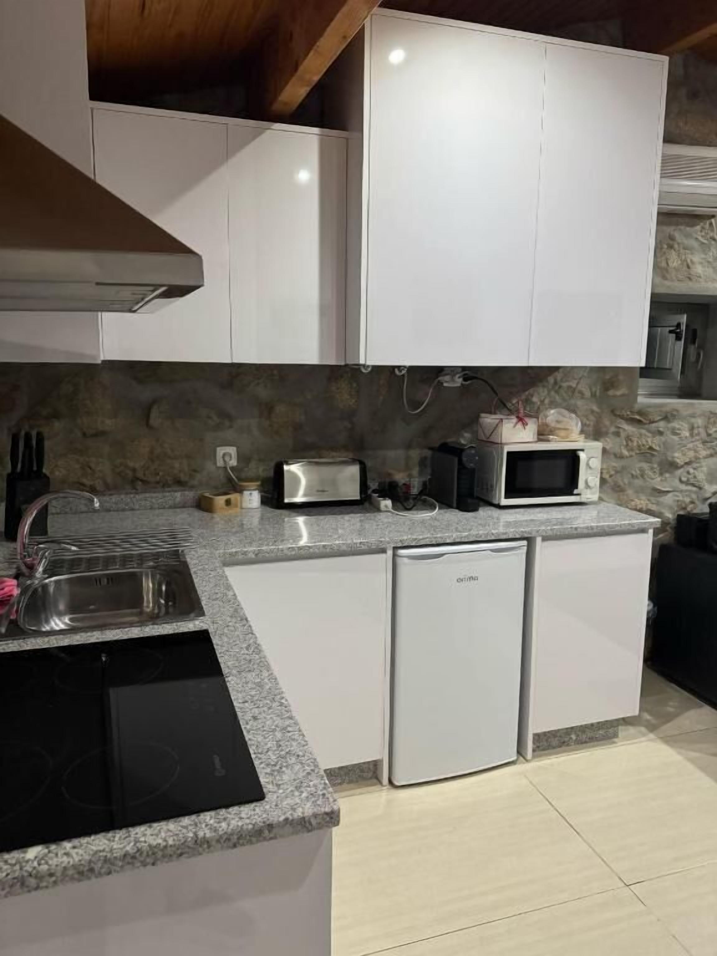 Una cocina compacta con armarios blancos, encimera de granito, lavavajillas integrado y salpicadero de piedra.