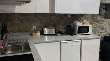 Una cocina compacta con armarios blancos, encimera de granito, lavavajillas integrado y salpicadero de piedra.