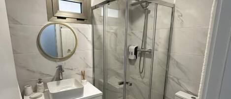 A modern bathroom with a glass-enclosed shower, a white sink, and a toilet.