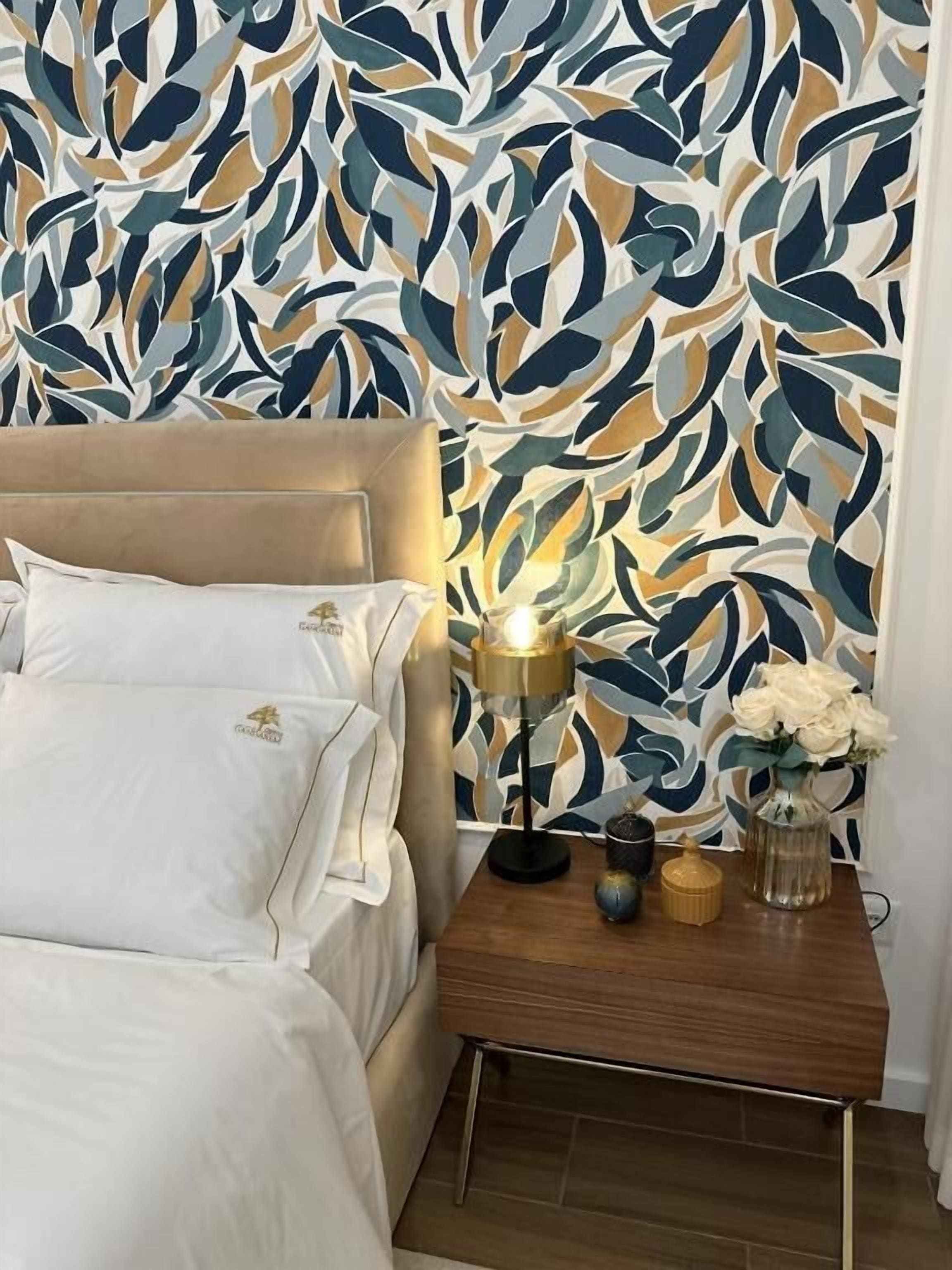 A bedroom with a bed, a bedside table with a lamp, and a decorative wall.