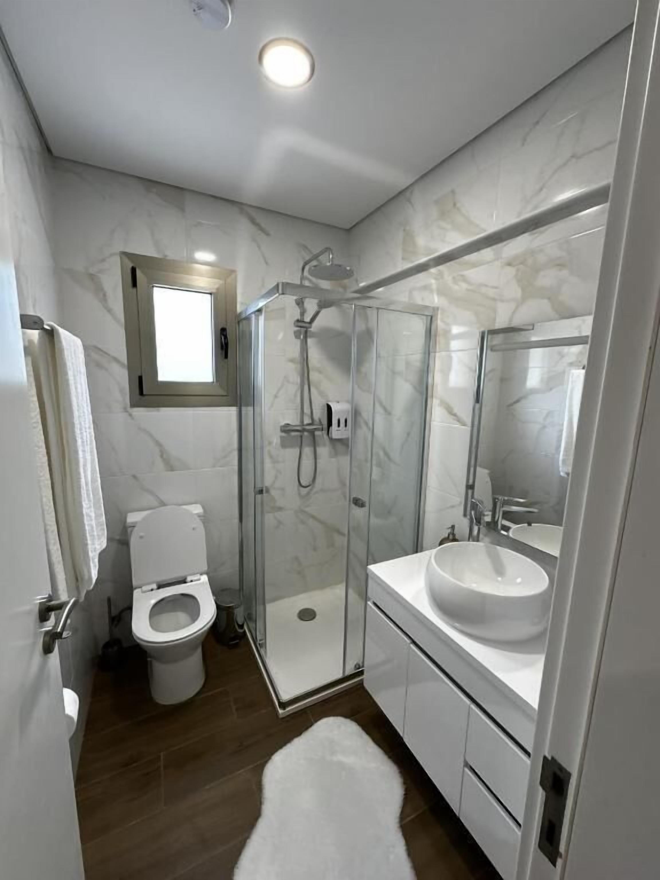 A modern bathroom with a glass-enclosed shower, a toilet, and a sink with a mirror.