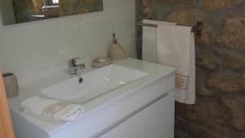 Un baño con pared de piedra, un lavabo blanco, un espejo y una toalla colgada en un perchero.