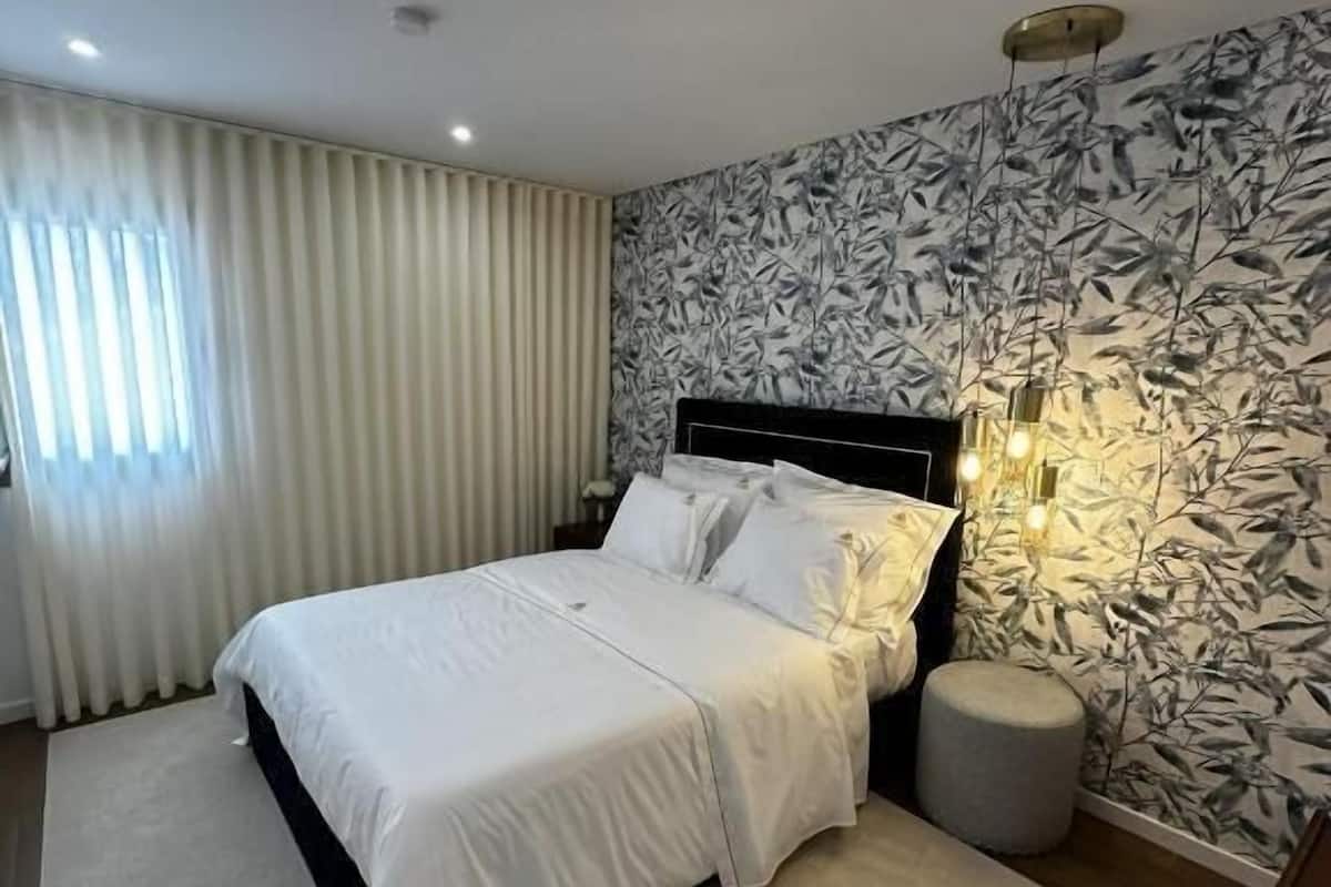 Une chambre à coucher avec un lit, un pouf rond et un mur orné d’un motif végétal.