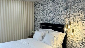 Ein ordentlich gemachtes Bett mit weißer Bettwäsche, ein runder Hocker und eine Wand mit einem Blattmuster.