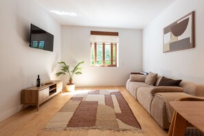A living room with a sofa, a television mounted on the wall, a wooden cabinet, a potted plant, and a window with a view of greenery. - Garça Real - Porto Retreat by Lisbeyond (Porto)
