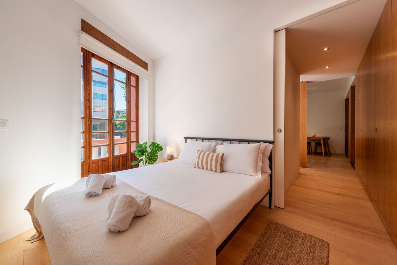 Ein Schlafzimmer mit einem großen Bett, Holzboden, einem Fenster mit Ausblick und einer Tür zu einem anderen Raum.